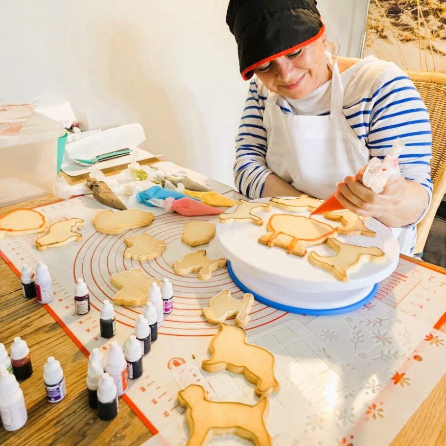 Ateliers culinaires en anglais Une personne décore des biscuits en forme d'animaux sur une table avec des colorants alimentaires.