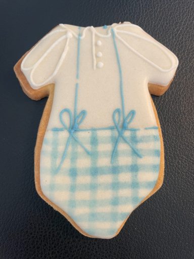Biscuit décoré bébé Biscuit en forme de grenouillère blanche avec des détails bleus en carreaux.