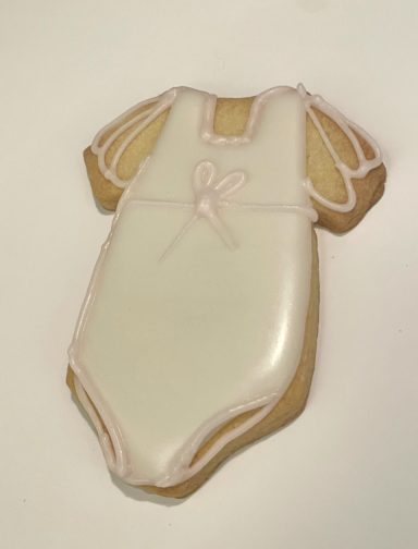 Body rosé Biscuits en forme de body de bébé, décorés de glaçage blanc et de détails roses.