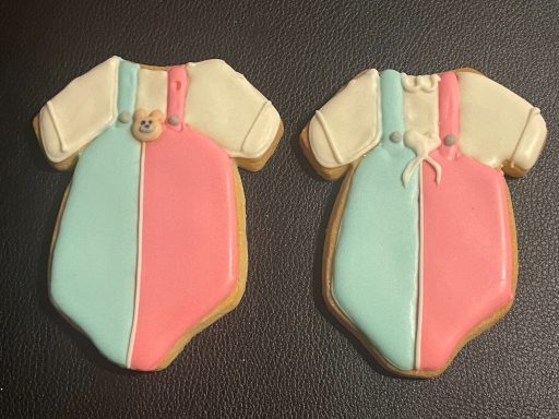 Gateaux évènementiels Gender reveal Deux biscuits en forme de grenouillère, l'un bleu et l'autre rose.